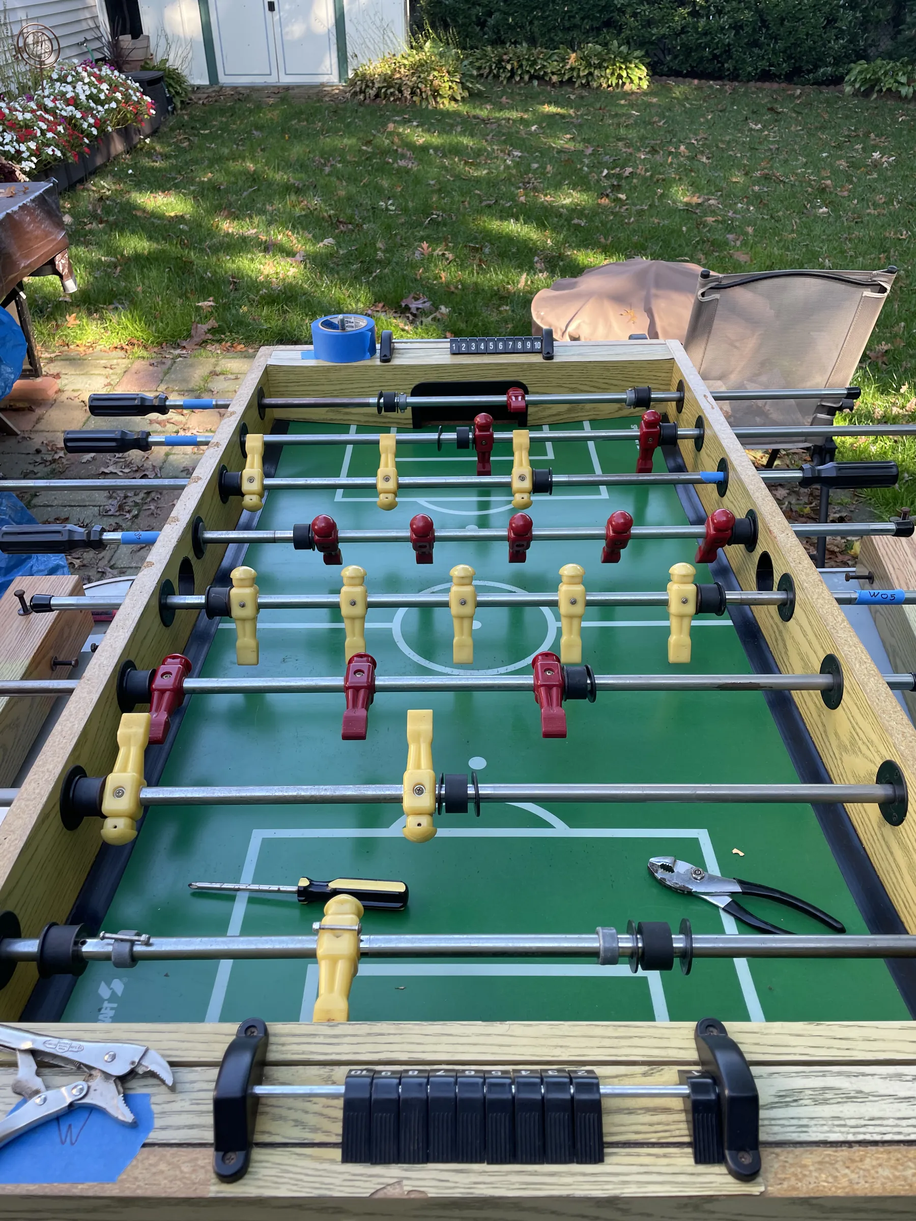 The foosball table outside on pickup day, part way through reassembly, with clamps, a screwdriver and pliers lying on the playfield